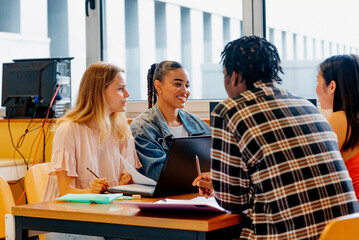 multiracial group of young man and women studying together with class notes and a laptop at the table in a university campus.