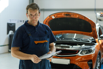 portrait of an experienced male auto mechanic against the background of a car with an open hood in...
