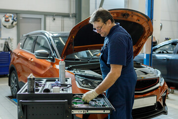 an experienced professional mechanic selects a tool in a cabinet with tools in a car repair service on the background of an SUV