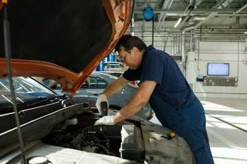 Fototapeta na wymiar auto mechanic under the hood with a screwdriver repairs the car