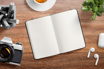 Top view of an opened blank hardcover leather notebook on a wood office desk table with  with pens, cup of coffee, earphone, vintage film camera and succulent plant. High resolution.