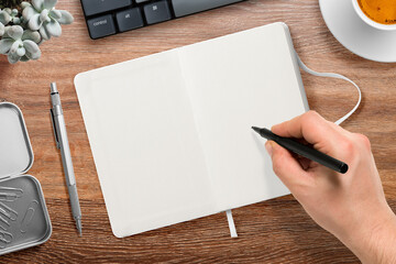 Top view of a male hand writing with a marker on a blank hardcover leather notebook on a wood...