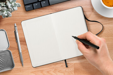 Top view of a male hand writing with a marker on a blank hardcover leather notebook on a wood...