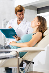 Obraz premium Friendly doctor holding document folder interacting attentively with adult woman lying on couch in clinic, gathering vital medical information and assessing patient health status