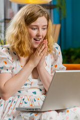 Surprised happy redhead young adult woman using laptop computer receive good news success message shocked by sudden victory celebrate lottery jackpot win purchases online shopping at home. Vertical