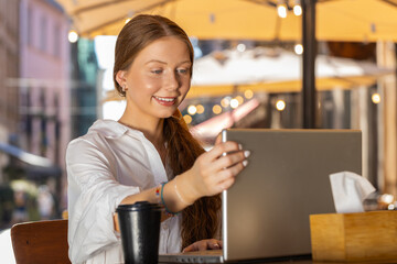 Pretty redhead child girl start begin work online distant job open laptop in city street cafe restaurant browsing website chatting outdoors during break. Young smiling woman tourist looking at camera