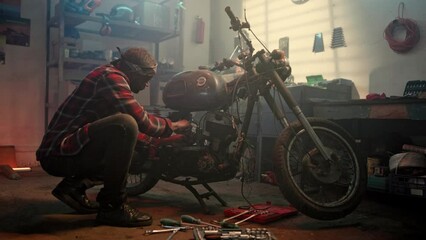 Mechanic servicing or repairing vintage retro motorbike in neat well equipped workshop. African american professional repairman working in garage. Maintenance service. Creative authentic workshop.