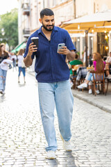 Happy indian man use smartphone typing text messages browsing internet social media web app working chatting online enjoying morning to-go coffee hot drink outdoor. Guy tourist walking in city street