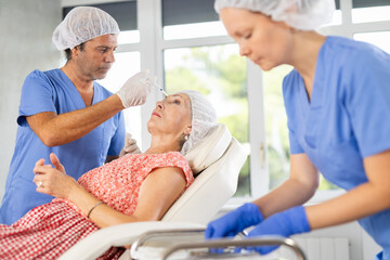 Obraz premium Senior woman applying rejuvenating treatments by mature male doctor in cosmetology office. Nurse preparing syringe.