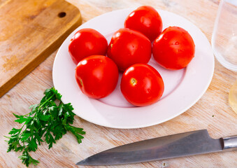Delicious ripe tomatoes on a plate, decorated with fresh parsley. Ingredients for cooking..