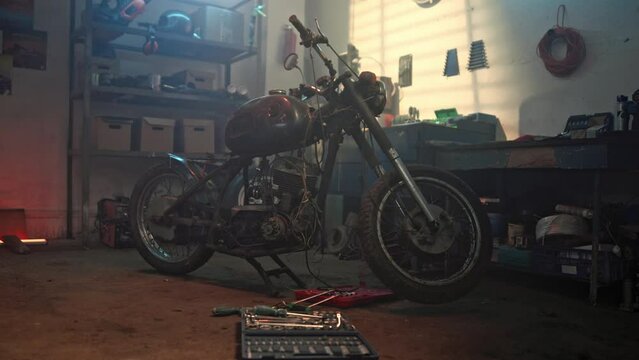Vintage style motorcycle in customs garage. Motorbike standing on service at authentic creative garage workshop. Mechanical hobby and repairs concepts. Creative authentic workshop. Hard manual work.