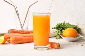 Glass of fresh carrot juice with parsley and orange on white wooden table