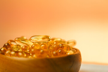 Fish oil capsules in a wooden cup on a blurred orange background.Omega fatty acids in jelly...