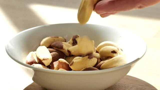 Brazil nuts cup on a wooden tablein .hand pours nuts into a plate.slow motion.Healthy fats.Brazil nuts in the diet.Nuts and seeds. 4k footage
