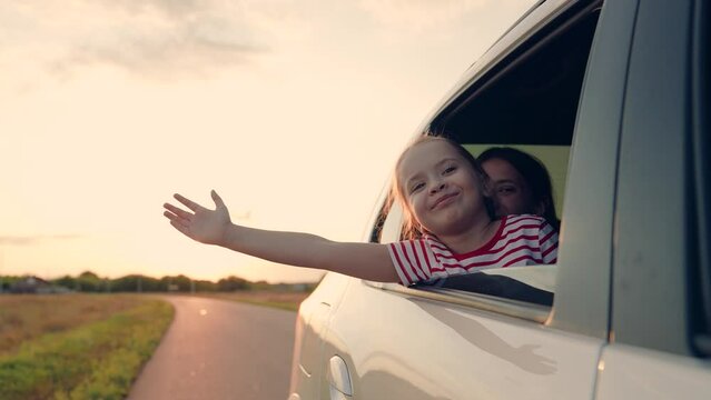 Little girl kid enjoys family trip by car. Child, stretching his hand out of car window, laughs. Girl child looks out of car window. Happy family travels by car. Child holiday emotion. Family vacation