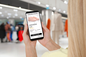 Woman visiting shop to take ordered shoes indoors, closeup. Online store website on device screen