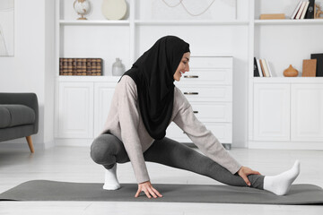 Muslim woman in hijab stretching on fitness mat at home