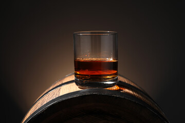 Glass of tasty whiskey on wooden barrel against dark background
