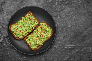 Slices of bread with tasty guacamole on black textured table, top view. Space for text
