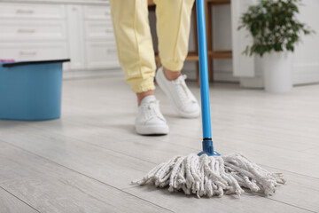 Woman cleaning floor with mop indoors, selective focus