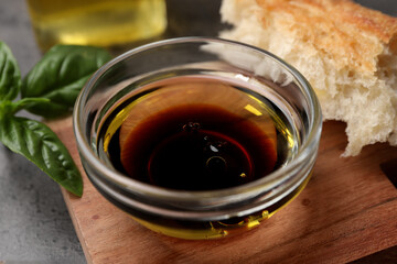 Bowl of organic balsamic vinegar with oil, basil and bread on grey table, closeup