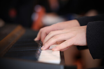 Close up of hands and fingers playing a keyboard or piano white keys. Audience blurred in...