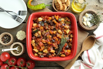 Dish with tasty ratatouille, ingredients and bread on wooden table, flat lay