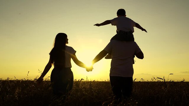 Mother father, little daughter enjoying nature together outdoor. People travel. Mom dad child walk hand in hand. Happy family of farmers with child, are walking on wheat field. Slow motion. Silhouette