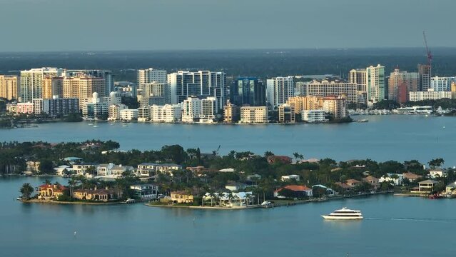 Expensive waterfront houses on Bird Key in Sarasota city in Florida, USA. Large cruise yacht siling on bay waters and high-rise office buildings in downtown district on horizon. Recreational pursuit
