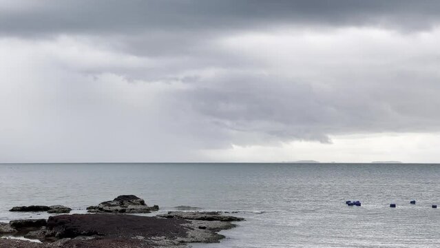 Cloudy weather before the rain at the tropical beach in rain season. Waves are crashing to the sandy coast. Dark grey storm clouds. Dramatic sky.