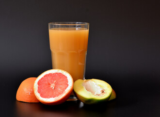 Refreshing fruit juice on a black background, next to the halves of ripe mango and grapefruit.