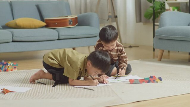 Full Body Of Asian Kids Sitting On The Floor In The Room With Plastic Toy Brick Drawing Together At Home

