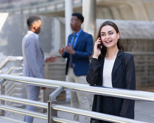 beautiful woman calling with customer with black businessmen talking togerther at background. businesswoman in black suit working outside building in city