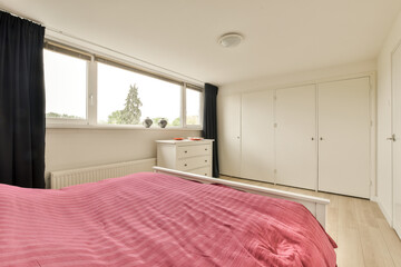 a bedroom with pink bedding and white cupboards on the wall next to the window in the room is empty
