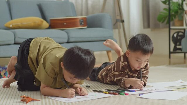 Close Up Of Asian Kids Lying On The Floor In The Room With Plastic Toy Brick Drawing Together At Home
