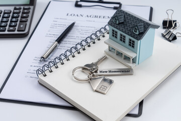 Classic house model, house key with "new homeowner" and calculator on office desk.