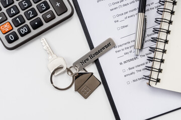 House key with "new homeowner" and calculator on office desk.