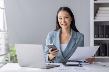 Portrait of young Asian businesswoman in suit, woman smiling and work at workplace inside office, accountant with calculator behind paper phone signing contracts and financial reports