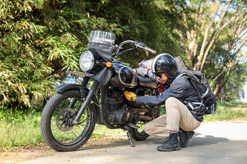Fototapeta na wymiar Man checking his motorcycle on the road. Motorcyclist checking engine of motorcycle and searching for malfunction