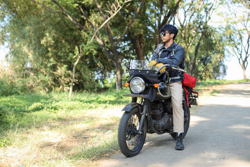 Fototapeta na wymiar Young Asian man having a rest after long journey on side of road while sitting on motorcycle