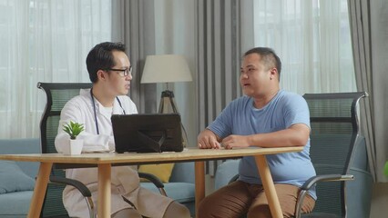 Asian Male Doctor With A Fat Male Patient In Clinic, Sitting At Desk, Discussing About The Results Of Medical Check Up On A Tablet, Giving Bad News, Encouraging A Patient
