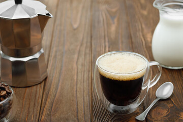 cup of espresso and geyser coffee maker and jug of cream on wooden table