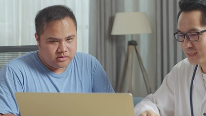 Close Up Of Asian Male Doctor With A Fat Male Patient In Clinic, Sitting At Desk, Discussing About The Results Of Medical Check Up On A Laptop, Giving Bad News, Encouraging A Patient
