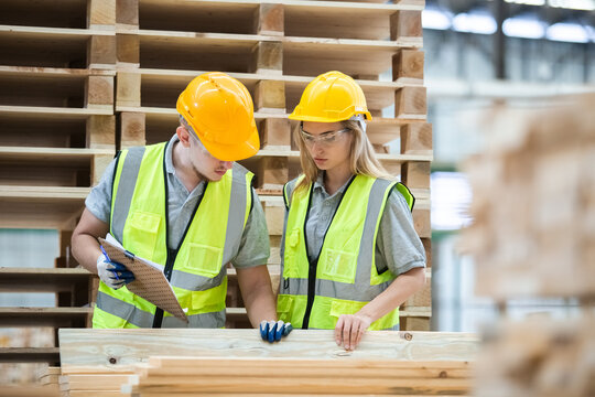 Team engineer carpenter wearing safety uniform and hard hat working holding clipboard checking quality of wooden products at workshop manufacturing. man and woman worker wood warehouse industry.