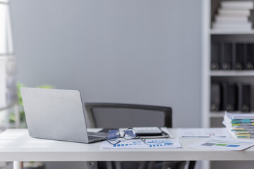 Laptop Computer, notebook, and eyeglasses sitting on a desk in a large open plan office space after working hours	