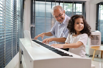 Happy smiling asian senior man sitting and playing piano while teaching grandchild in living room house indorrs. Musical and relaxation makes elder male happiness. Health care lifestyle concept.