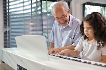 Happy smiling asian senior man sitting and playing piano while teaching grandchild in living room house indorrs. Musical and relaxation makes elder male happiness. Health care lifestyle concept.