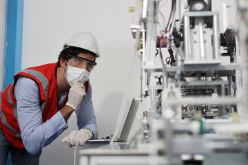Caucasian mechanic technician maintenance, repairing industrial machinery equipment in factory. Professional worker in protective clothing with computer and mask using wrench at manufacturing factory