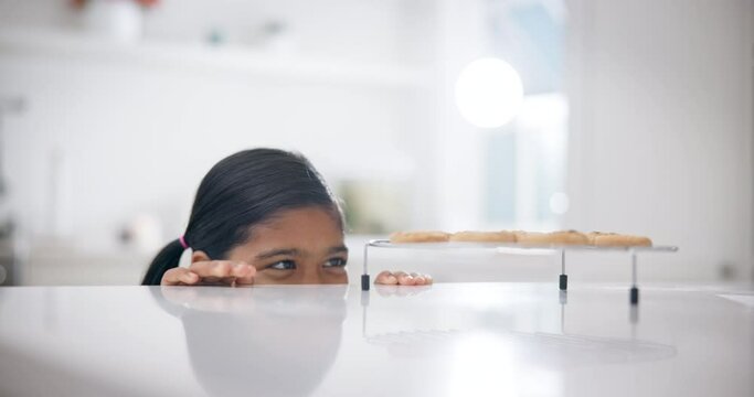 Naughty, sneaky and a child for a cookie in the kitchen for food, dessert or hungry. Smile, looking and a young girl on the counter for a snack craving, eating biscuit or a sweet treat after baking