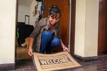  Happy young woman placing a welcome doormat in her new apartment in moving in day   